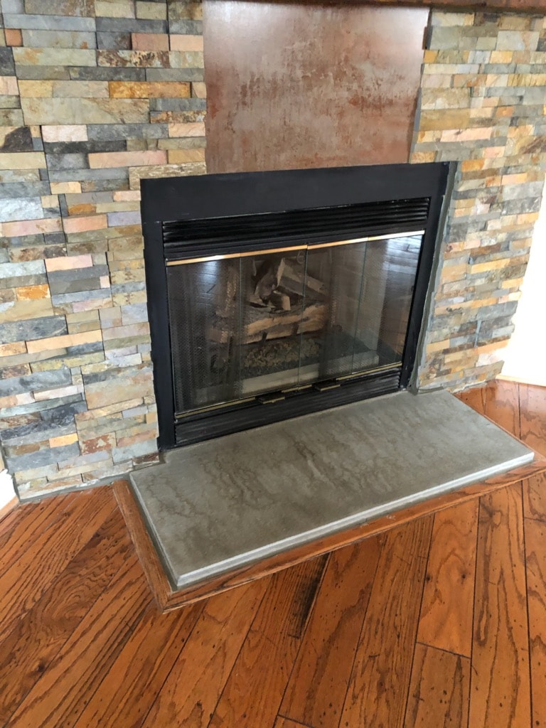 Norstone Ochre Stacked Stone Rock Panels on a corner fireplace with vertical metal insert and small concrete hearth step